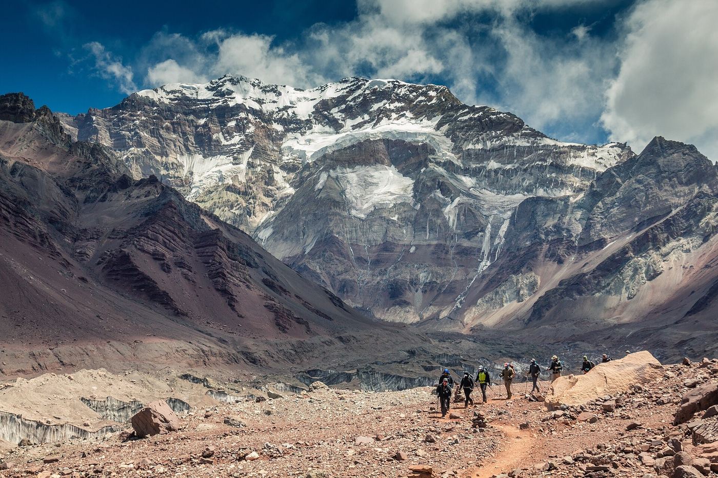 Grupo de excursionistas caminando por un sendero de piedra frente a la pared sur del Aconcagua