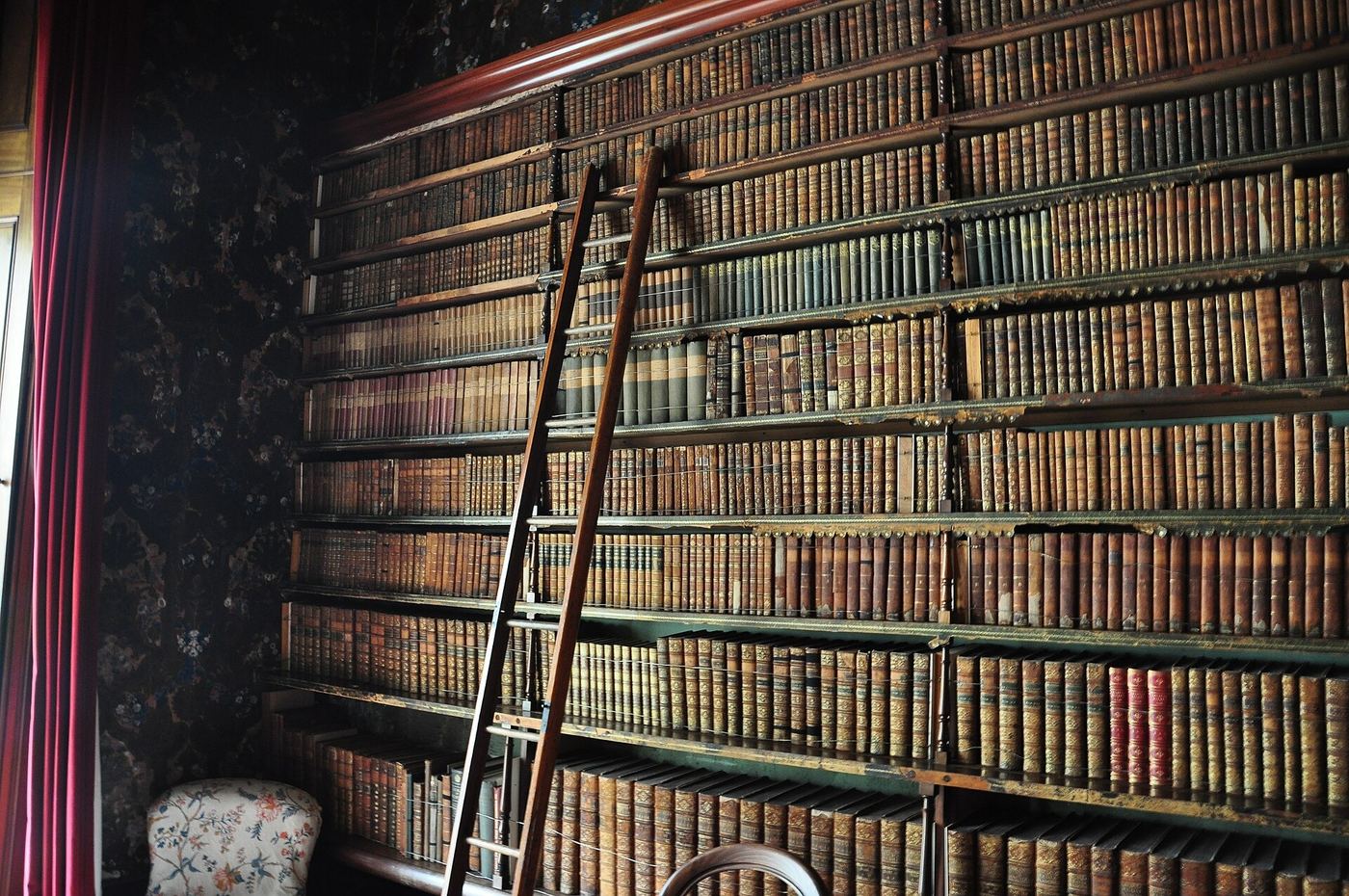 Biblioteca con libros antiguos de lomo de cuero y escalera de madera