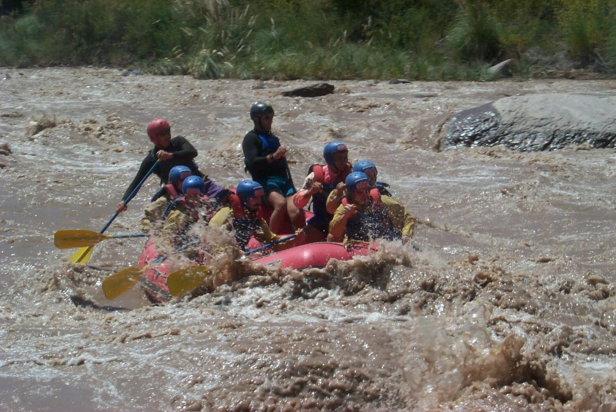 Balsa con remeros y cascos atravesando aguas marrones y rápidas del Río Mendoza